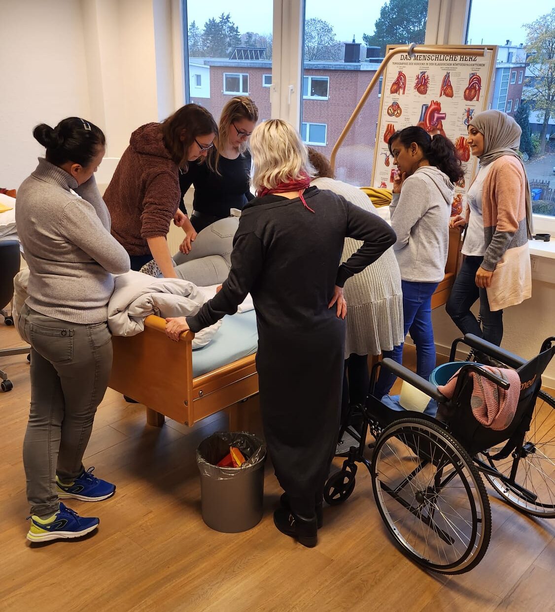 Eine Gruppe von Personen stehen um ein Pflegebett herum und lernen wie die Lagerung im Bett funktioniert.